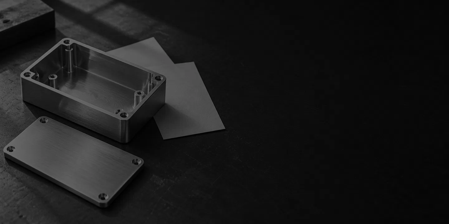 Greyscale conceptual metal enclosure and detached lid beside blank review cards on a dark engineering desk.