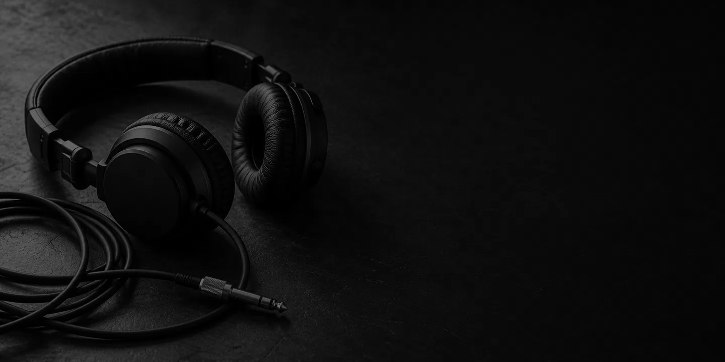 Greyscale conceptual unbranded on-ear headphones beside a coiled audio cable and metal jack on a dark desk.