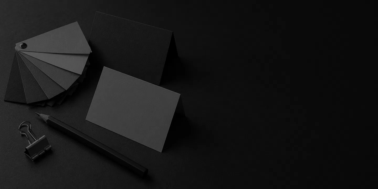 Greyscale conceptual paper swatches, blank folded cards, pencil and plain binder clip on a dark design desk.