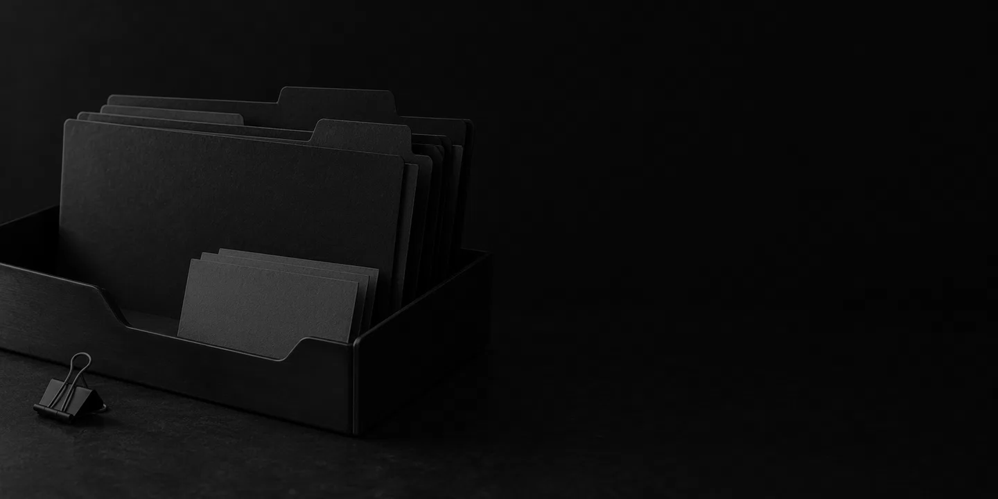 Greyscale conceptual document tray with plain charcoal folders, blank index cards and a metal binder clip on a dark desk.