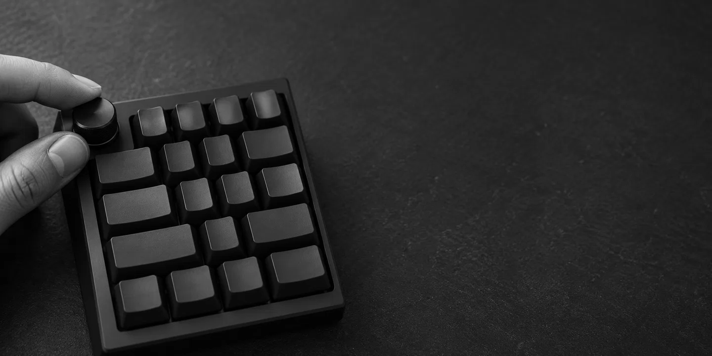 Greyscale conceptual close-up of a hand at the rotary control of an unbranded keyboard.