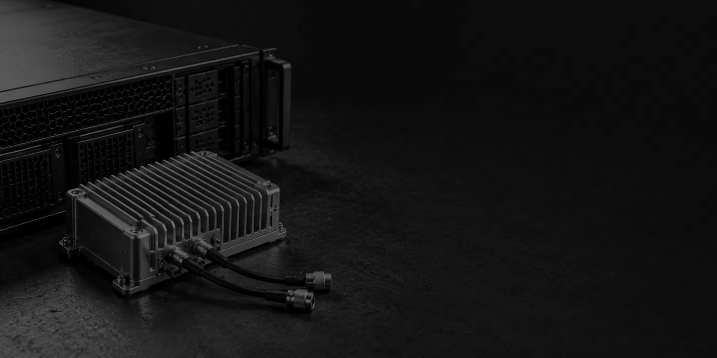 Greyscale conceptual finned radio module with two short coaxial cables beside an unbranded server on dark slate.
