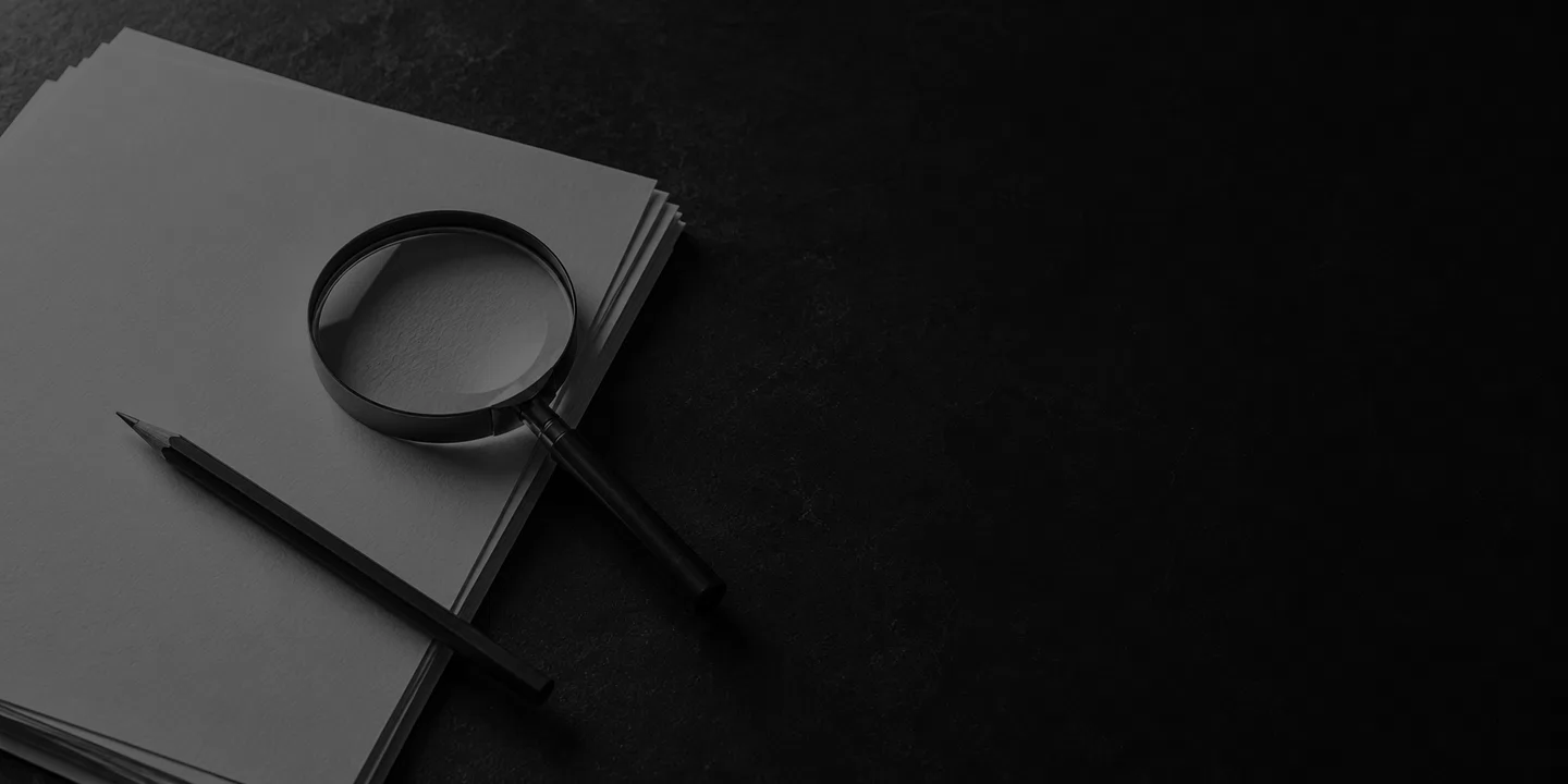 Greyscale conceptual blank paper sheets, graphite pencil and magnifying glass arranged on the left of a dark writing desk.